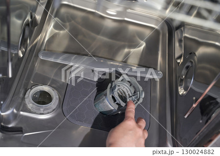 Female hand cleaning stainless steel dishwasher filter inside open appliance 130024882