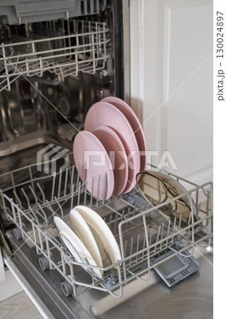 Open dishwasher with pink plates and white bowls in modern kitchen interior Open dishwasher with pink plates and white bowls in modern kitchen interior 130024897