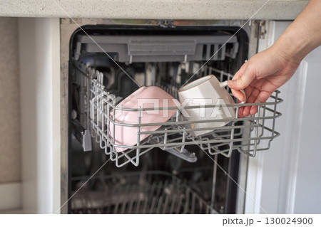 Female hand loading cups into dishwasher for cleaning in modern kitchen setting 130024900