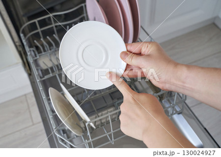 Caucasian adult female loading dishwasher with saucer in modern kitchen setting Caucasian adult female loading dishwasher with saucer in modern kitchen setting 130024927