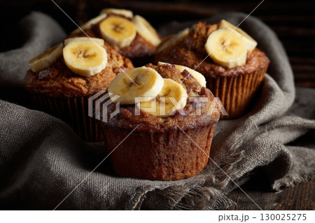 Banana cupcakes. Golden-brown freshly baked cupcakes topped with banana slices and brown sugar. Banana muffins on parchment paper against a rustic wooden background. Breakfast treat. Homemade dessert. 130025275