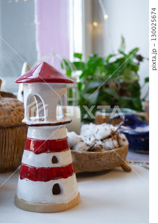 elegant ceramic craft lighthouse among decorative items in an indoor setting. vertical. closeup. elegant ceramic craft lighthouse among decorative items in an indoor setting. vertical. closeup. 130025674