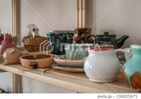 ceramic craft variety handmade pottery on wooden shelves in cozy workshop setting. closeup. ceramic craft variety handmade pottery on wooden shelves in cozy workshop setting. closeup. 130025675