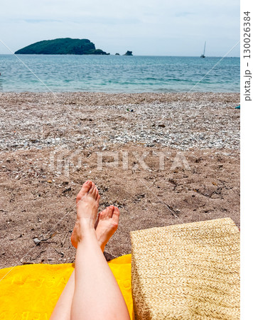 Bare feet on a yellow towel at the seaside beach with island view. Relaxation, vacation and lifestyle freedom by the ocean coast. 130026384