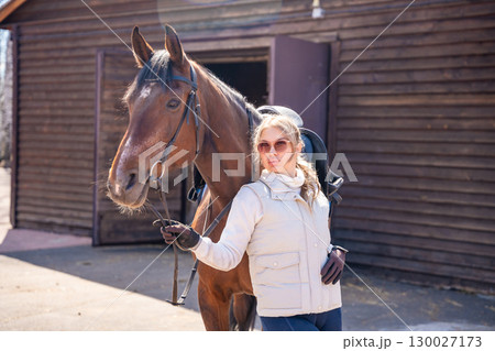 Portrait of a young woman with a horse at a rustic farm. Concept of rural lifestyle and countryside elegance. Portrait of a young woman with a horse at a rustic farm. Concept of rural lifestyle and countryside elegance. 130027173