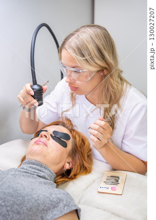Eyelash extension procedure using ultraviolet lamp in modern beauty salon. Innovative lash enhancement technology with precise application technique. 130027207