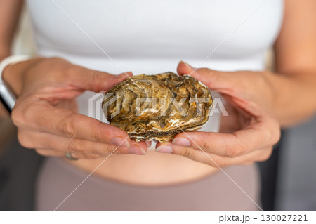 Close-up of an oyster in a woman hands at home. Symbol of nutrition benefits and female health support. Close-up of an oyster in a woman hands at home. Symbol of nutrition benefits and female health support. 130027221