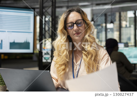 Female business manager reviewing project agenda for progress on her laptop, preparing a strategic report at workstation. General director showcasing determination for career progression. Female business manager reviewing project agenda for progress on her laptop, preparing a strategic report at workstation. General director showcasing determination for career progression. 130027437