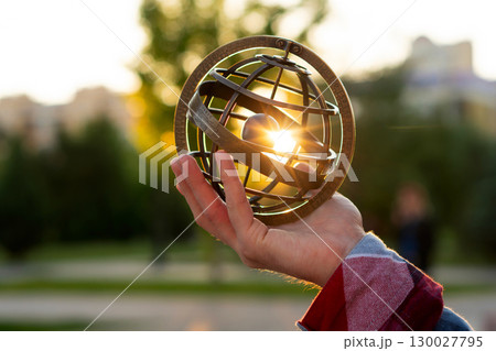 Hand holding armillary sphere capturing bright sunset in park 130027795