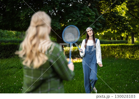 Friends enjoying a playful badminton match in a sunny park setting 130028103
