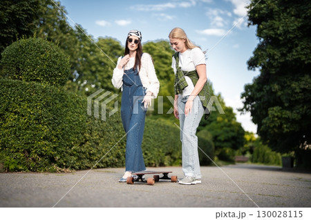 Friends enjoy a sunny day skateboarding together in a lush park 130028115