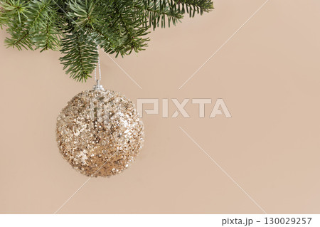 Christmas hanging shiny beige bauble on fir snowy branch on beige background. Xmas greeting card. New Year concept. Copy space. Close up. 130029257