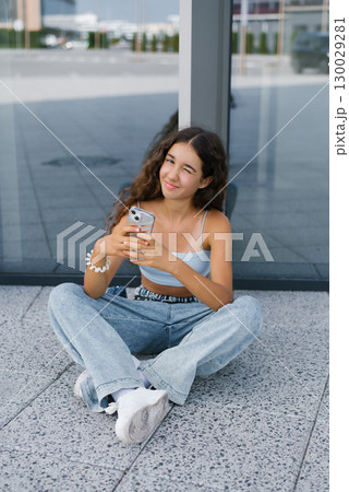 Smiling Teen With Smartphone Relaxing On Pavement 130029281
