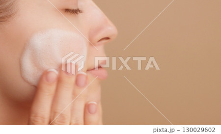 Close-up of a beautiful female face. Woman applying cleansing foam gently washing face ads. Bubbles. Beauty daily routine. Commercial shoot. Skincare treatment. Selfcare. Copy space. Beige Background Close-up of a beautiful female face. Woman applying cleansing foam gently washing face ads. Bubbles. Beauty daily routine. Commercial shoot. Skincare treatment. Selfcare. Copy space. Beige Background 130029602