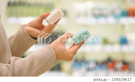 Woman selecting solid soap or shampoo bar in a beauty or eco store. Female customer comparing ingredients of natural products for face, body, hands or hair. Concept of sustainable choice, zero waste. 130029617
