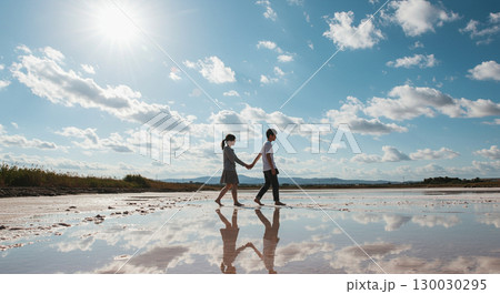 鏡のように反射する塩湖で手をつなぐ二人 130030295