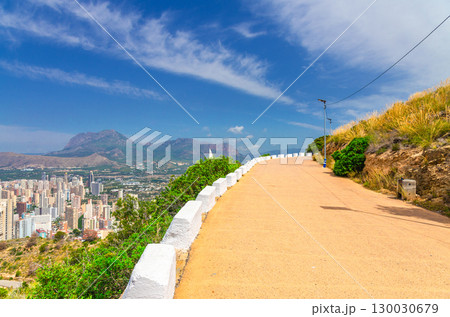 Mountain road serpentine on slope Serra Gelada natural park with aerial view of Benidorm city with skyscrapers, hotel buildings and Puig Campana mountain Sierra Cortina in summer day, Spain Mountain road serpentine on slope Serra Gelada natural park with aerial view of Benidorm city with skyscrapers, hotel buildings and Puig Campana mountain Sierra Cortina in summer day, Spain 130030679