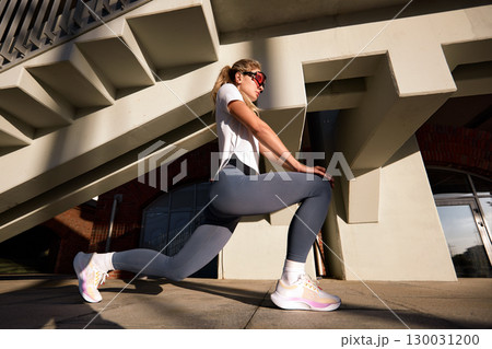 Athletic woman stretching outdoors beneath modern architectural structure Athletic woman stretching outdoors beneath modern architectural structure 130031200