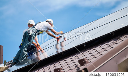 Workers building photovoltaic solar panel system on rooftop of house. Men technicians in helmets installing solar module with help of hex key outdoors. Alternative, renewable energy generation concept 130031993