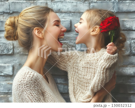 Joyful mother and daughter sharing laughter while holding a red rose 130032312