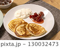 Freshly baked pancakes on the ceramic plate next to the strawberry jam and sour cream 130032473