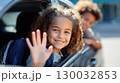 Smiling girl with backpack waving happily from car window on a sunny day 130032853