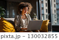 Smiling woman with headphones working on laptop at home in cozy modern interior 130032855