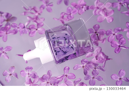 A bottle of serum with petals in water with lilac flowers. A bottle of serum with petals in water with lilac flowers. 130033464
