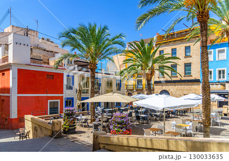 Multicolored typical buildings old houses, palm trees and street restaurant on Plaza del Quijano square in old town Alicante city historical centre in sunny summer day, Valencian Community, Spain 130033635