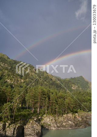 Double rainbow over lush forest mountain landscape under cloudy sky in serene 130033679