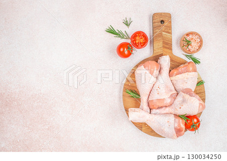 Raw chicken drumsticks on wooden board with tomatoes rosemary and salt. top view. copy space 130034250