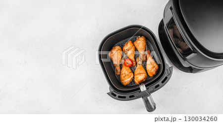 Cooked chicken drumsticks in air fryer basket with tomato and herbs. top view. copy space 130034260