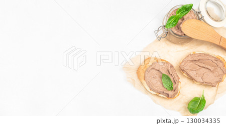 Toasted bread with creamy liver pate and fresh basil leaves on parchment. Long banner format. top view. copy space 130034335