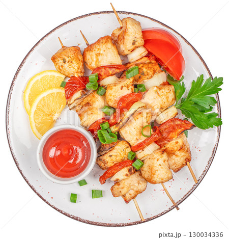 Grilled chicken skewers with vegetables, lemon slices, and sauce on white plate. 130034336