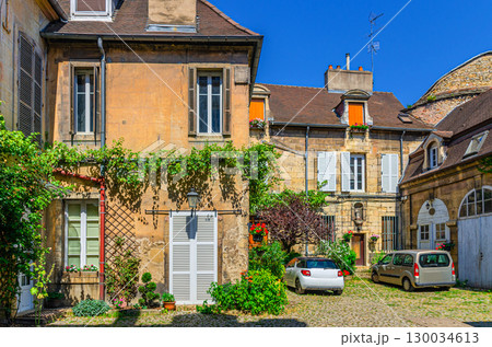 Typical small courtyard with hanging green plants on wall of old medieval houses and cars parking, typical french courtyard in Dijon city historical centre, Bourgogne-Franche-Comte region, France Typical small courtyard with hanging green plants on wall of old medieval houses and cars parking, typical french courtyard in Dijon city historical centre, Bourgogne-Franche-Comte region, France 130034613