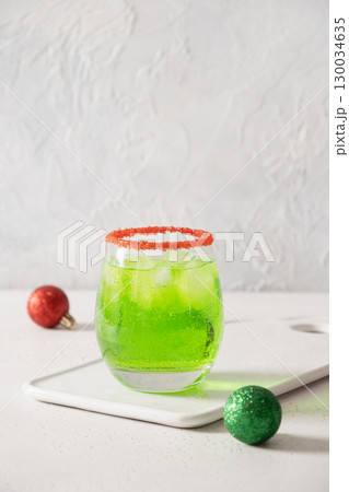 Xmas Green Punch in glass decorated red sugar rim on white table make of cool lime sherbet. Tasty drink for Christmas holiday. Rim your festive beverages in red sugar. Close up. 130034635