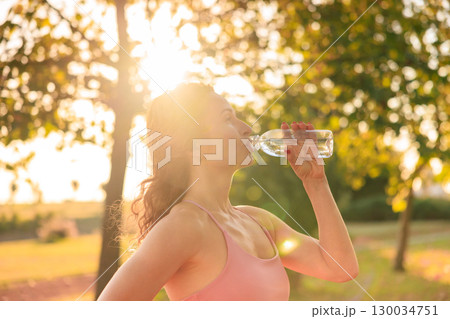 Fit sportswoman drinking water outdoors in autumn park Fit sportswoman drinking water outdoors in autumn park 130034751