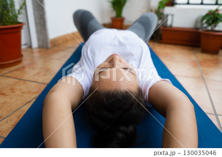 Person Practicing Relaxation Techniques on Yoga Mat at Home with Potted Plants Person Practicing Relaxation Techniques on Yoga Mat at Home with Potted Plants 130035046