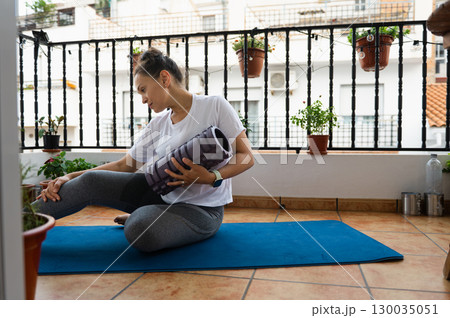 Woman Practicing Yoga on Balcony with Yoga Mat and Foam Roller 130035051