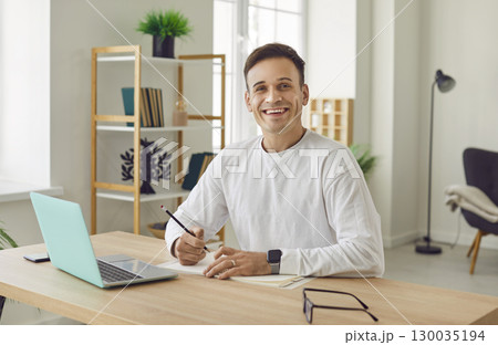 Portrait of young attractive business man working on a laptop and looking cheerful at camera. Portrait of young attractive business man working on a laptop and looking cheerful at camera. 130035194