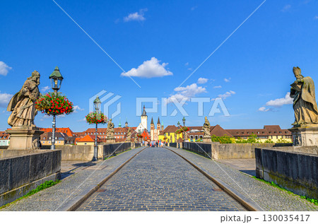Old Main Bridge Alte Mainbrucke with statues of saints, street lights and flowers, medieval buildings in Wurzburg old town altstadt, city historical center Mitte, Lower Franconia region, Germany 130035417