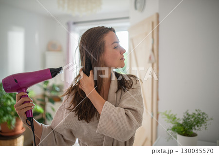 Woman blow-drying her hair after a relaxing bath. Woman blow-drying her hair after a relaxing bath. 130035570