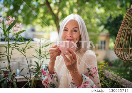 Portrait of beautiful senior woman standing on balcony, drinking coffee. Portrait of beautiful senior woman standing on balcony, drinking coffee. 130035715