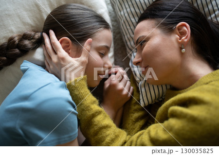 Top view of girl and mom talking in bed, lying face to face. Top view of girl and mom talking in bed, lying face to face. 130035825