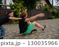Mother Pushing Son on Skateboard in Suburban Neighborhood Street 130035966