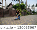 Mother Pushing Son on Skateboard in Suburban Neighborhood Street 130035967