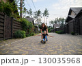 Mother Pushing Son on Skateboard in Suburban Neighborhood Street 130035968