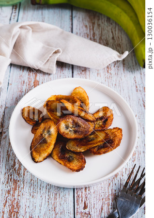 Tajadas fried banana on a plate on the table vertical view Tajadas fried banana on a plate on the table vertical view 130036154