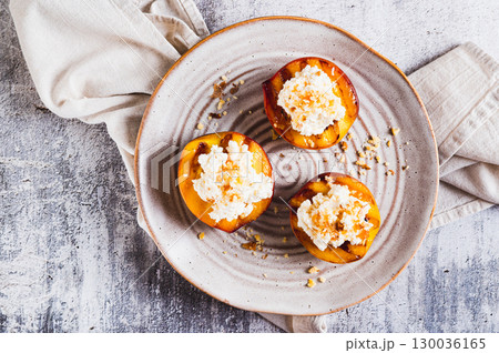 Close up of grilled peach halves with ricotta and nuts on a plate on the table top view Close up of grilled peach halves with ricotta and nuts on a plate on the table top view 130036165