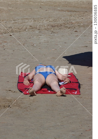 Woman sunbathing on red towel at beach holding smartphone 130036885